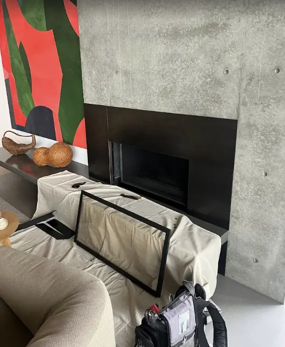 A modern fireplace in a concrete wall with its glass front removed and a drop cloth over the bench and sofa