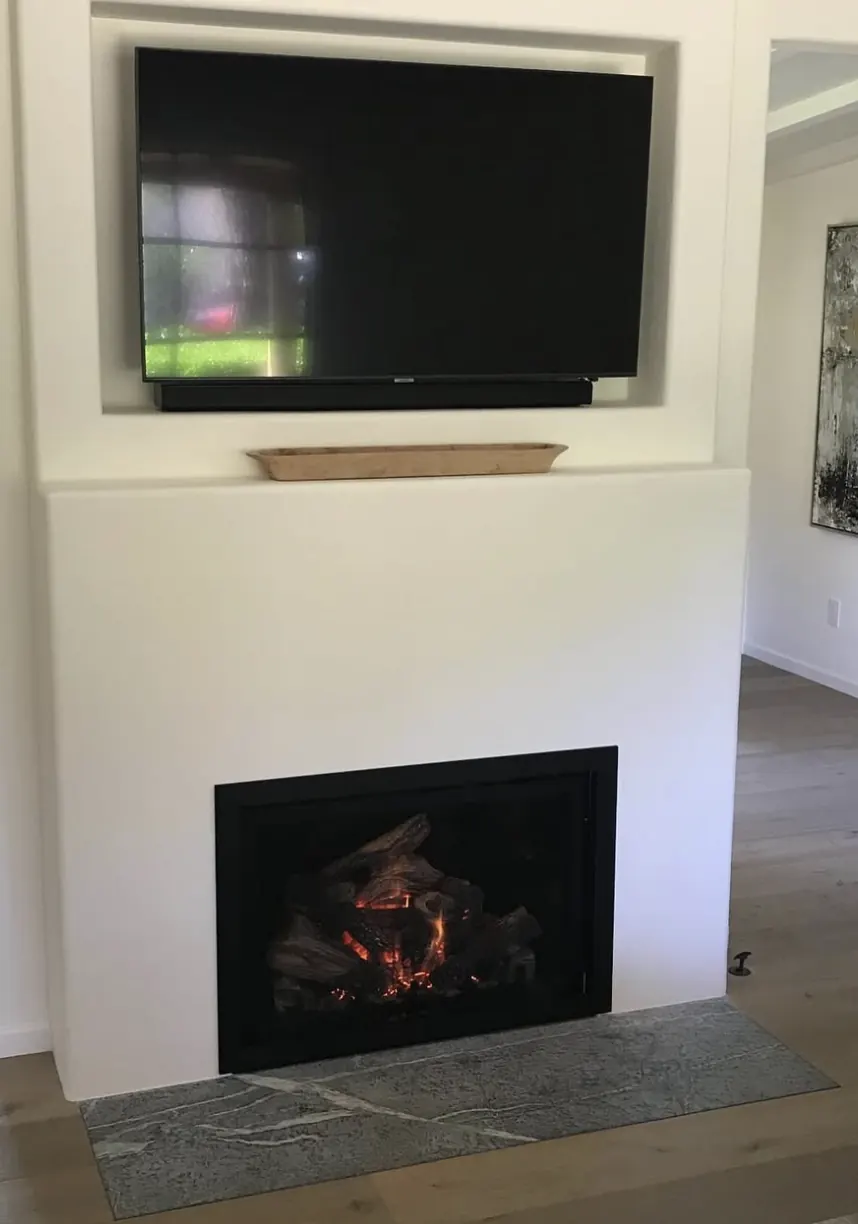 A gas insert in a white plaster surround with a stone hearth and a television above