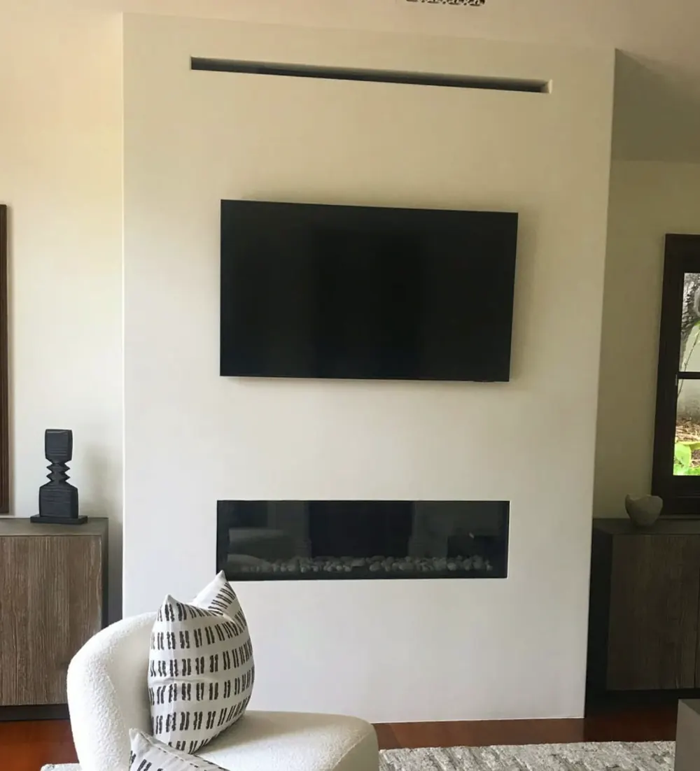 A linear fireplace set low in a white plaster wall beneath a wall mounted television