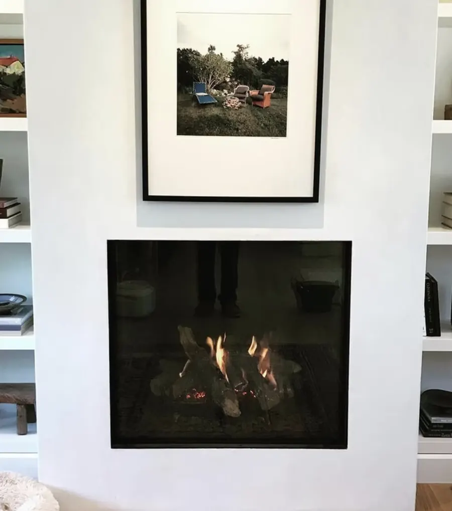 A square clean face gas fireplace in a white wall between bookshelves