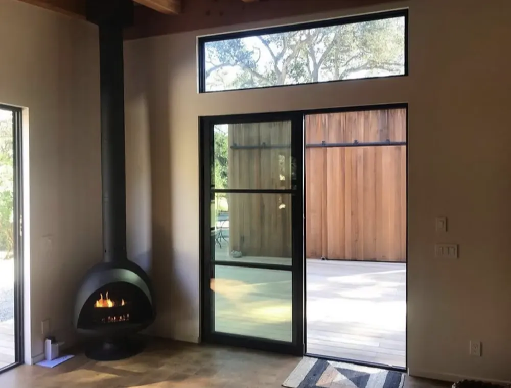 A black freestanding fireplace with a tall flue in the corner of a room with steel doors