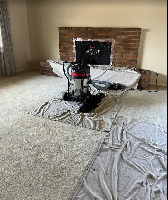 A brick fireplace sealed off for a sweep, with a vacuum and drop cloths across the carpet