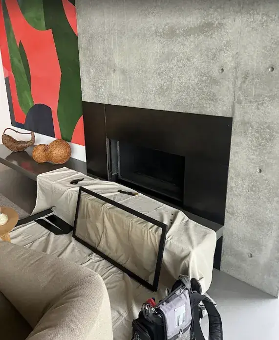 A modern fireplace in a concrete wall with its glass front removed and a drop cloth over the bench and sofa