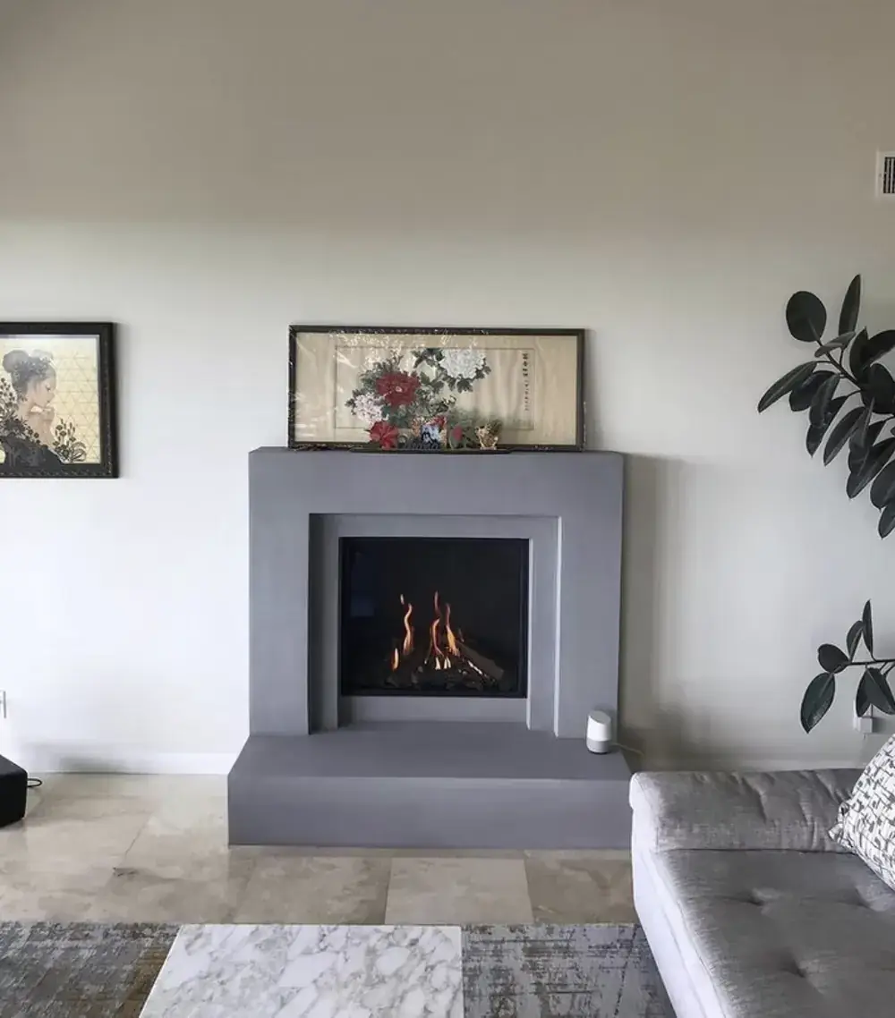 A gas fireplace burning in a grey plaster surround with a raised hearth in a living room