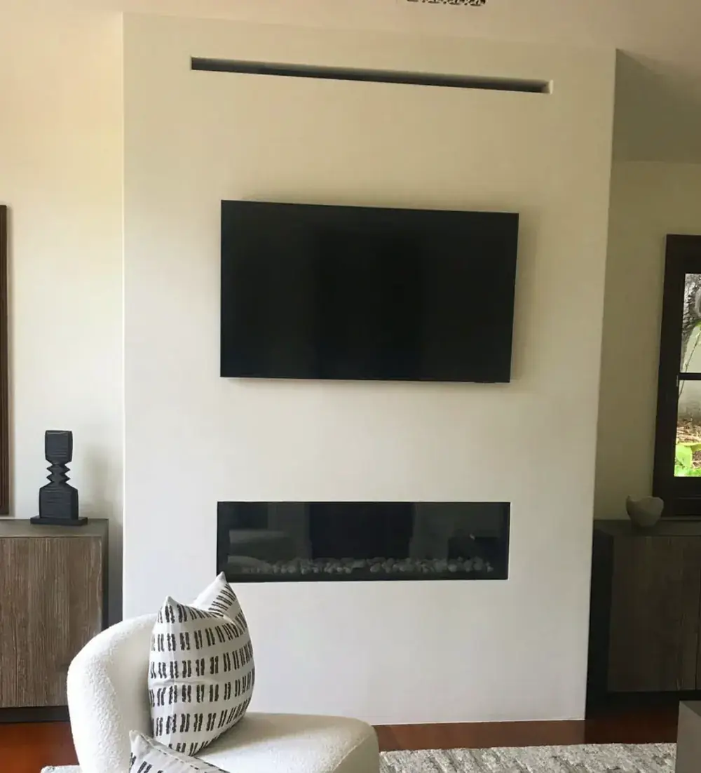 A linear fireplace set low in a white plaster wall beneath a wall mounted television
