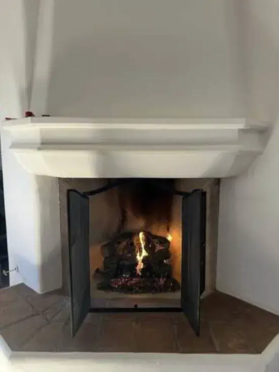 Gas logs burning in a white plaster corner fireplace with a tile hearth