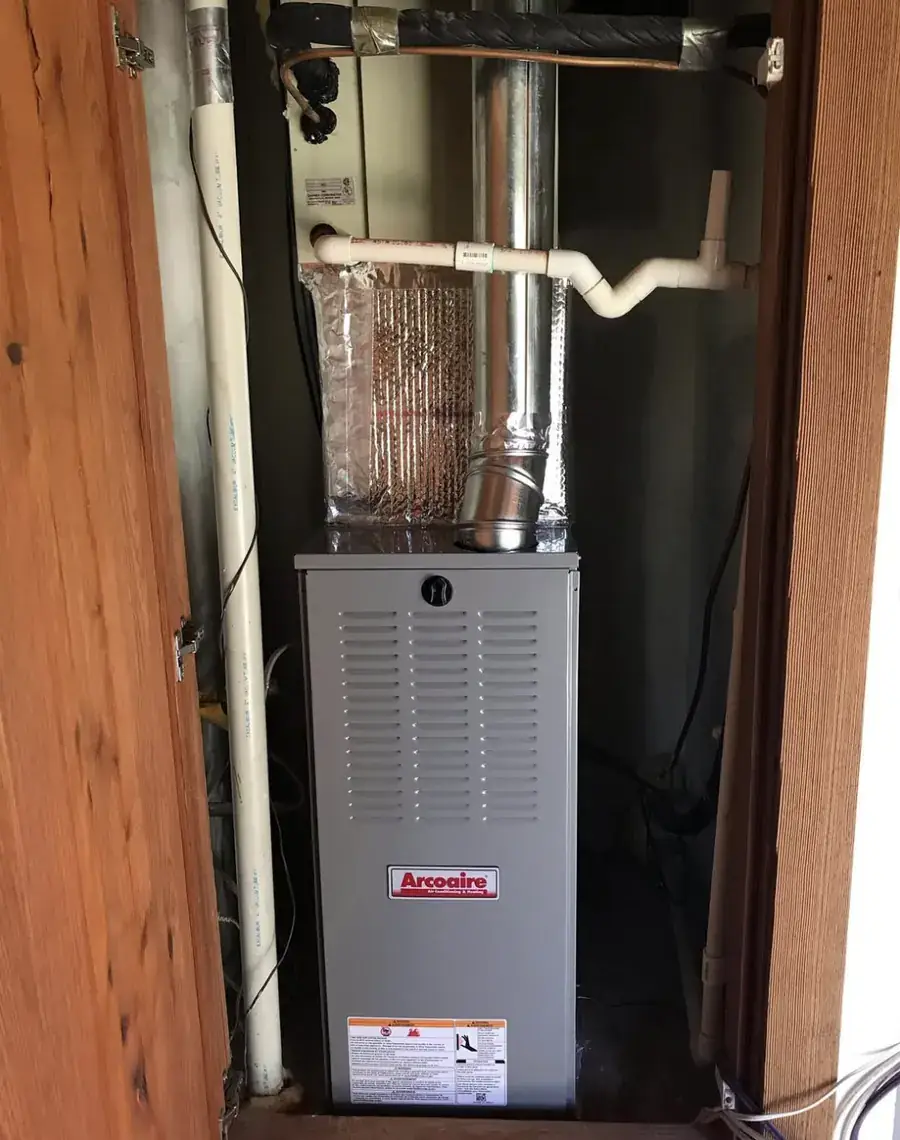 A new Arcoaire furnace installed in a narrow wood framed closet with its flue and drain lines