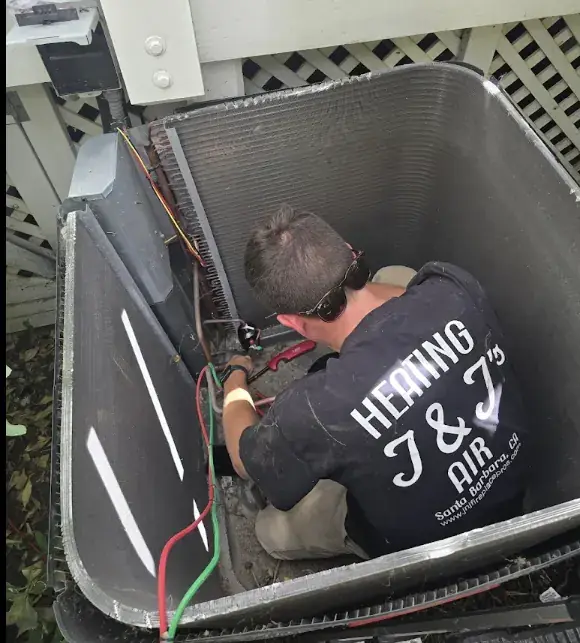 A technician in a J and J shirt working inside an opened outdoor condenser