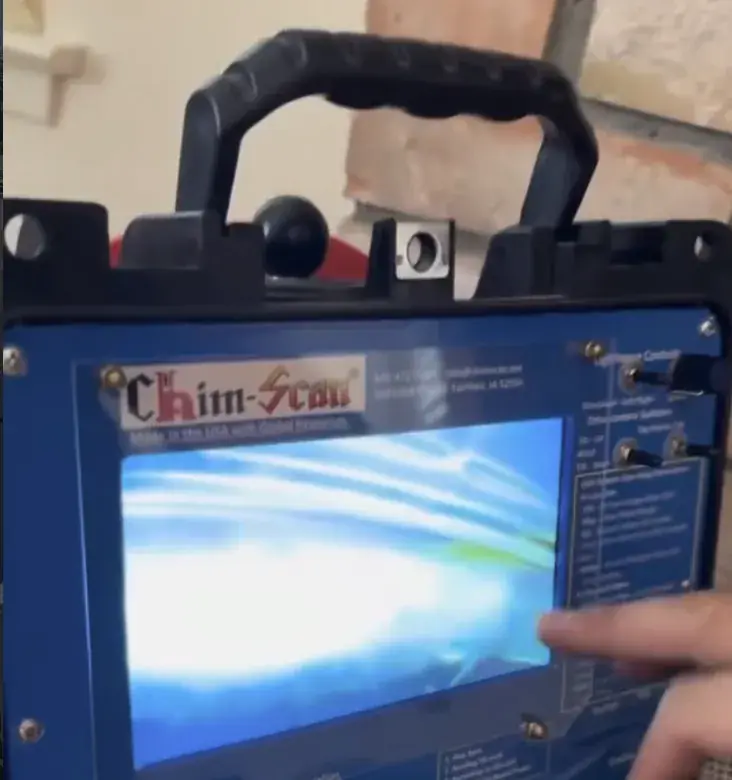 A chimney inspection camera unit with its screen lit, set up in front of a brick fireplace