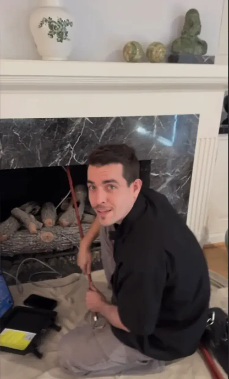 Jeremy Varela kneeling on a drop cloth at a marble fireplace, feeding the inspection camera up the flue