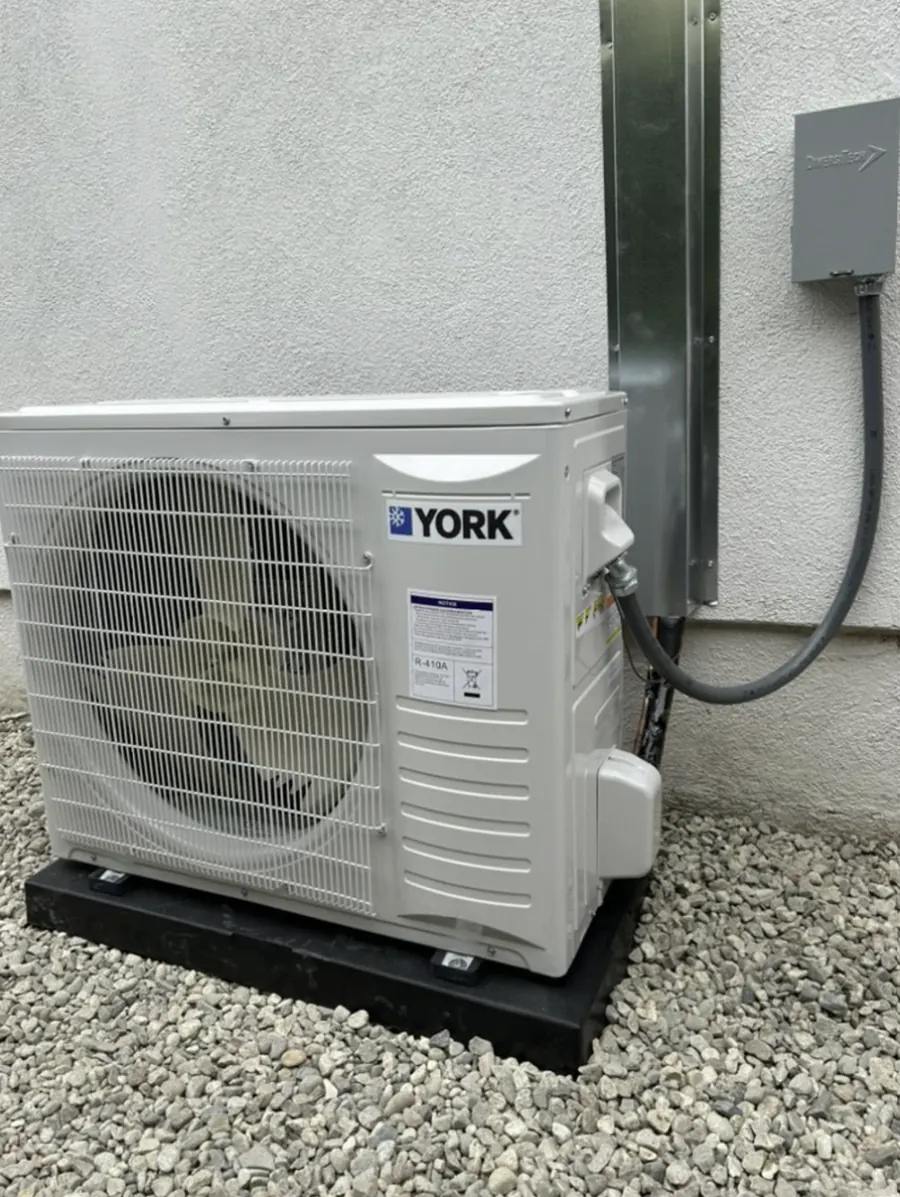 A York outdoor unit mounted on a pad against a stucco wall with its line set covered
