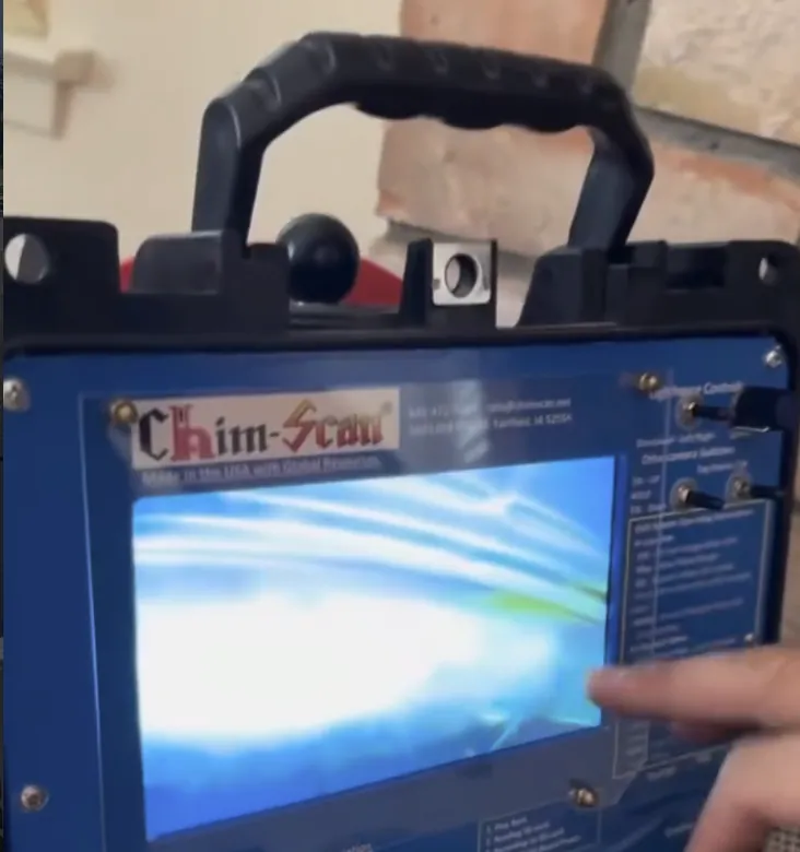 A chimney inspection camera unit with its screen lit, set up in front of a brick fireplace