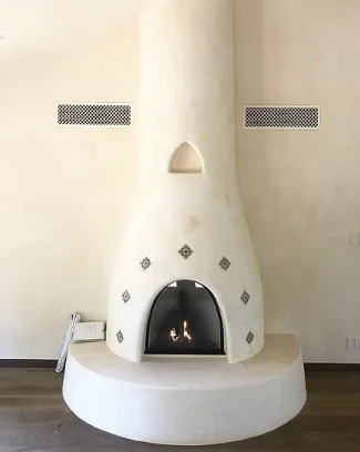 The same kiva fireplace finished in smooth white plaster with tile accents and a lit fire