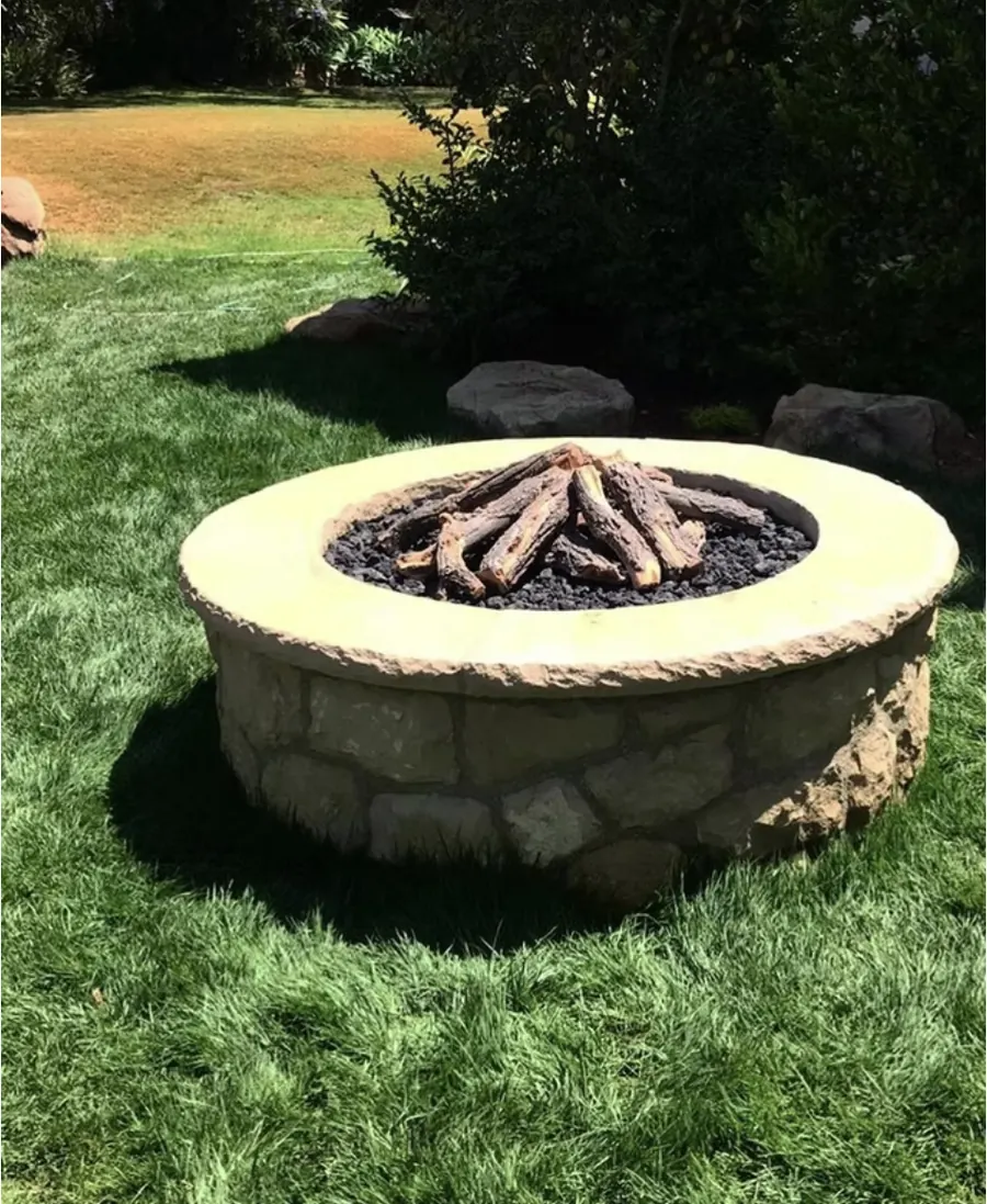 A round stone fire pit with a log set on a lawn