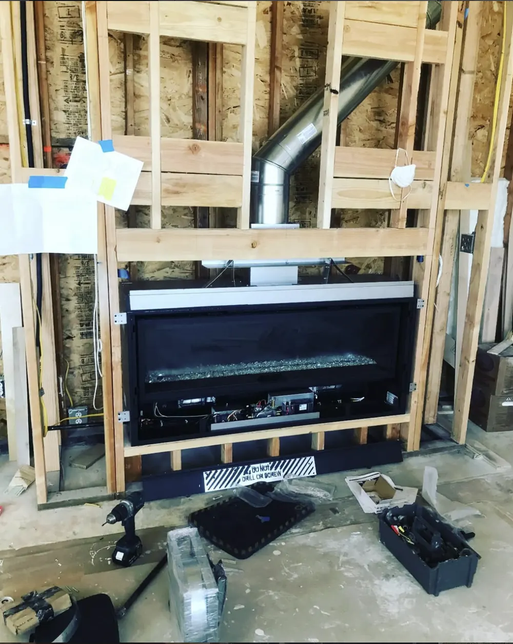 A linear gas fireplace mounted in wall framing with its vent pipe angled up through the studs