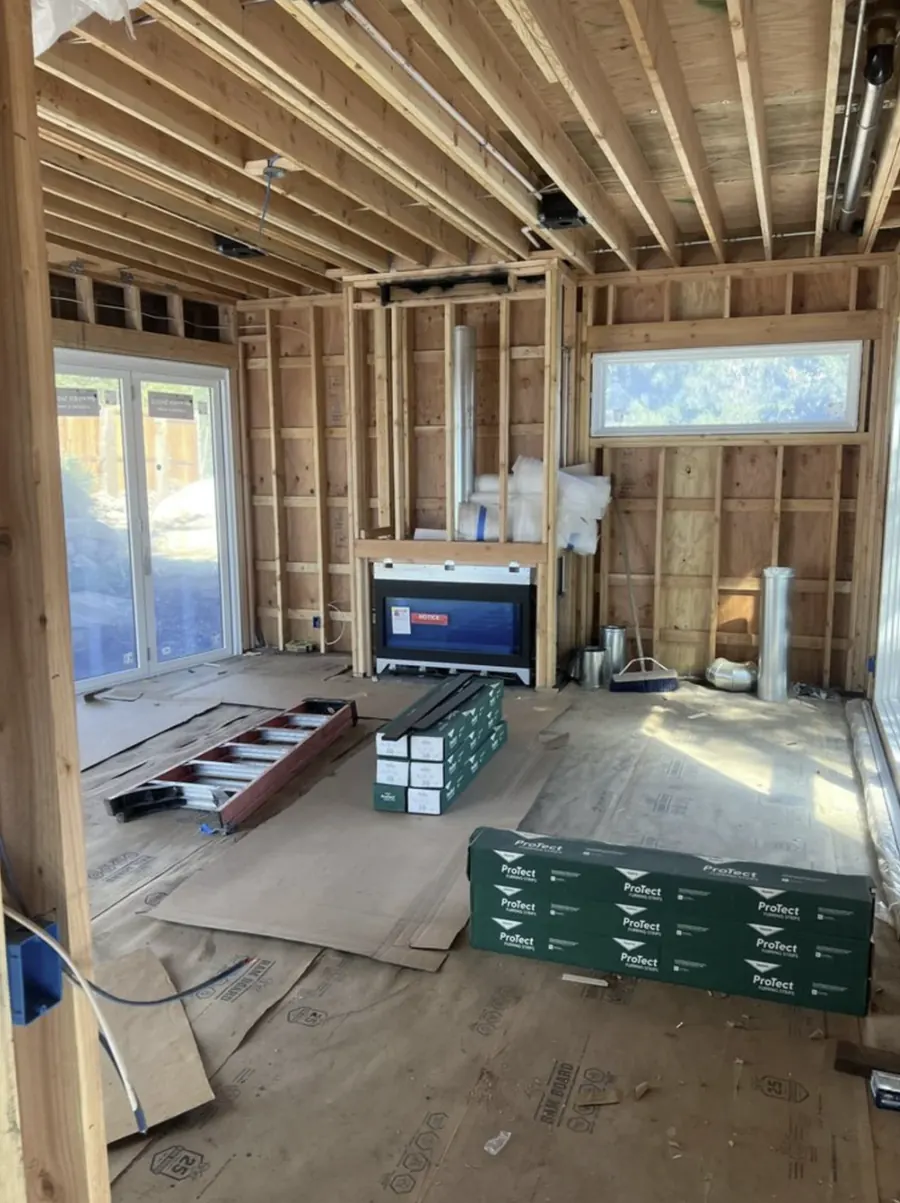 A framed room with a fireplace and vent pipe installed in the far wall before drywall